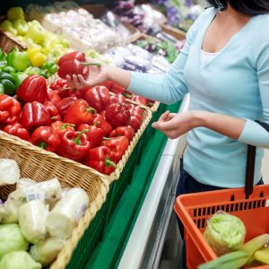 sale, shopping, food, consumerism and people concept - woman with basket buying bell peppers or paprika at grocery store